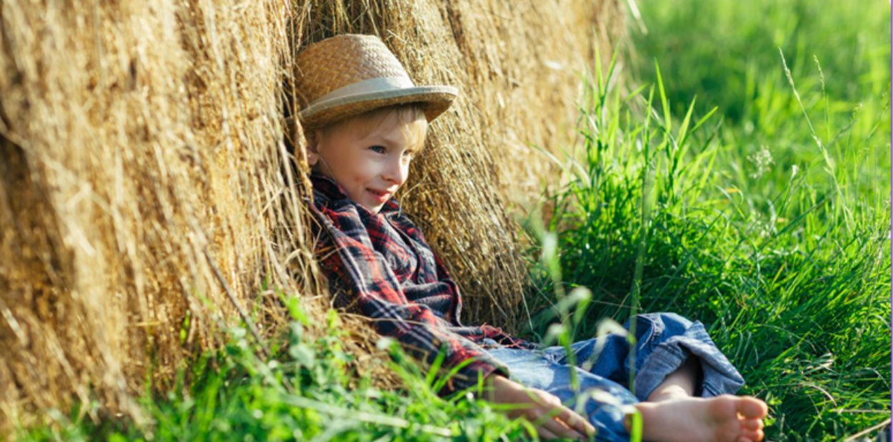 Child laying in a field against a bale of hay